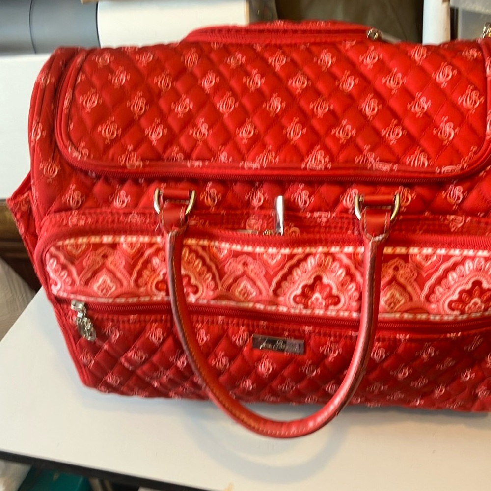 Red Vera Bradley weekender with handle and wheels. Measures 18” by 14” by 10”.